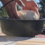 Photo of hands holding shaped bread dough and laying it into a dutch oven